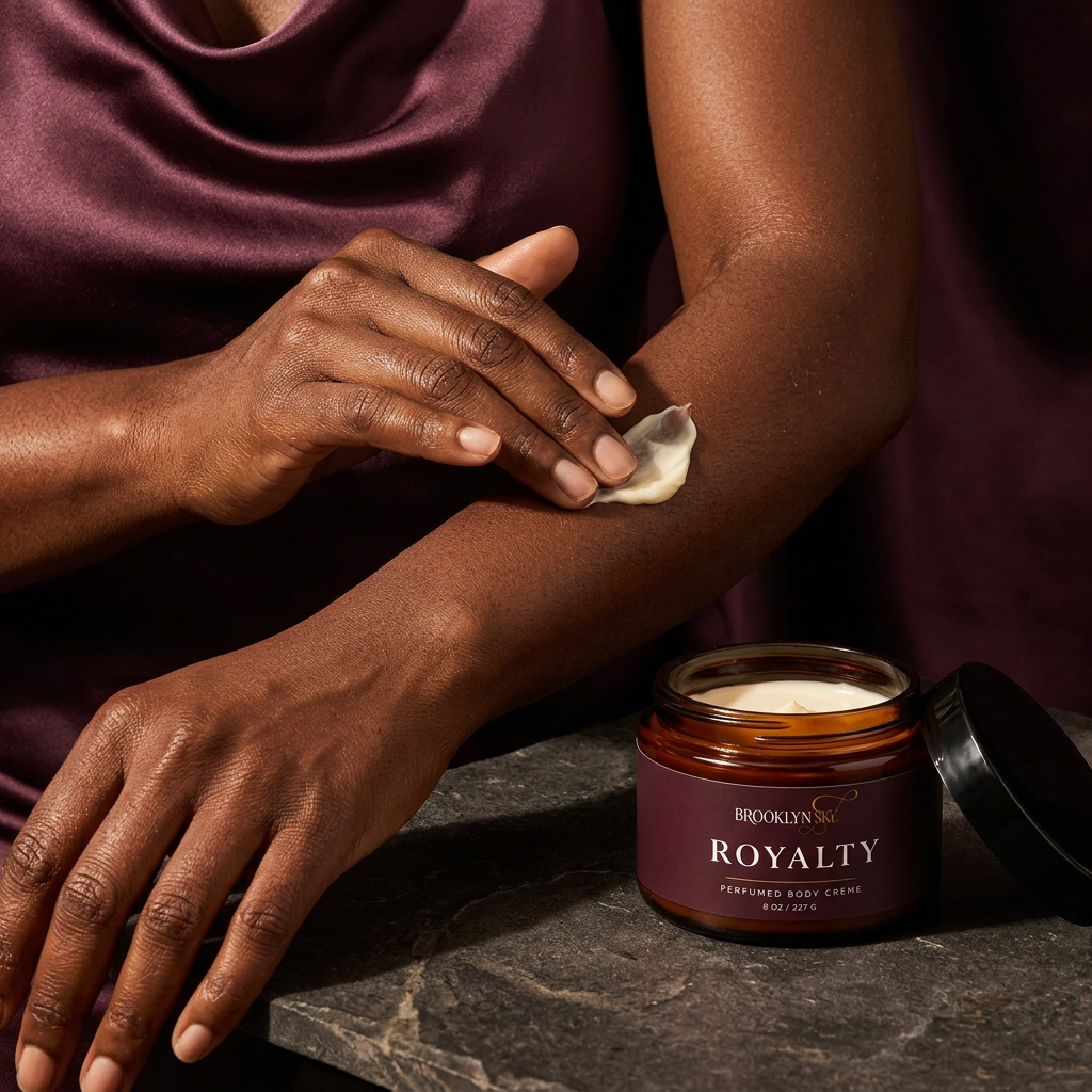 Woman massaging ivory body cream onto her forearm beside an open Royalty Body Crème jar.