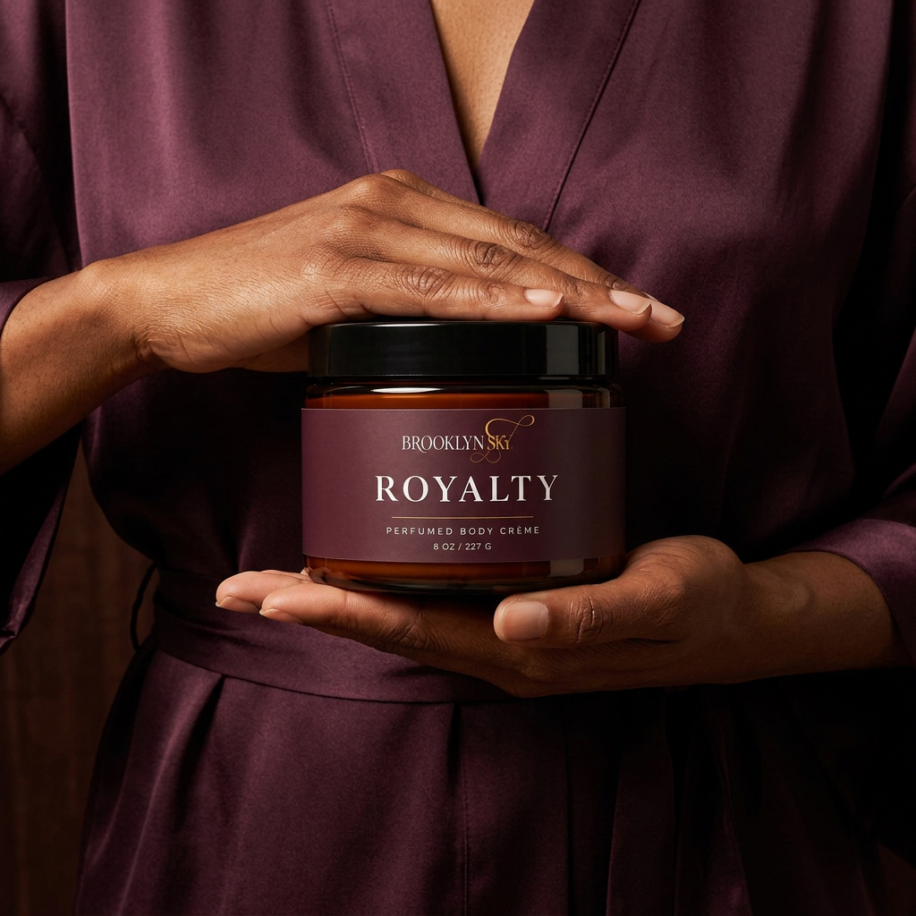 Woman in a plum robe holding a closed Royalty Body Crème jar between her hands.