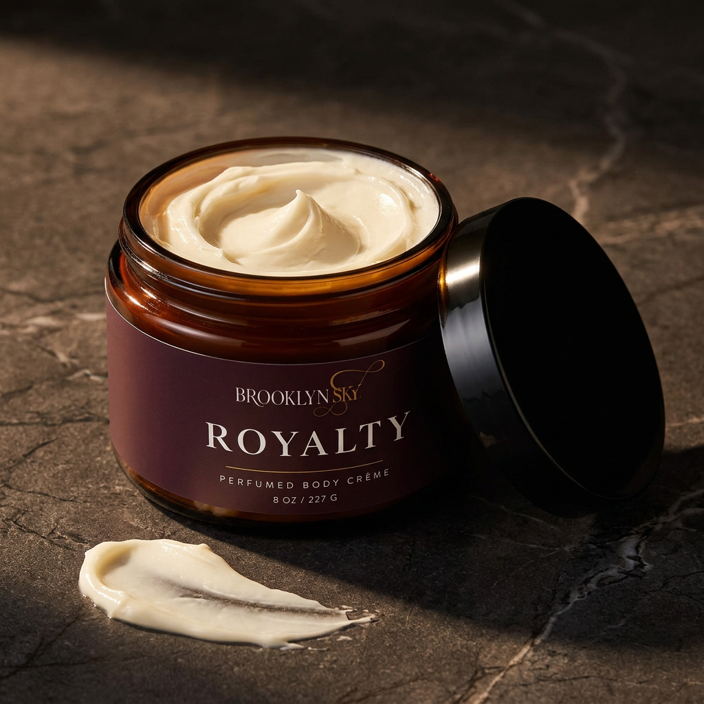 Open Royalty Body Crème jar showing ivory cream, with a cream swipe and black lid on dark stone.